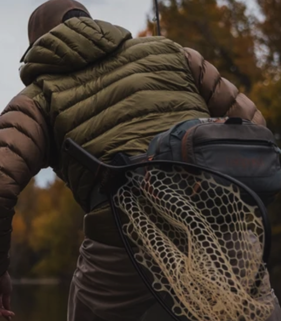 Angler carrying a landing net with the Broder Net Clip mounted behind the hip for secure hands-free fly fishing access
