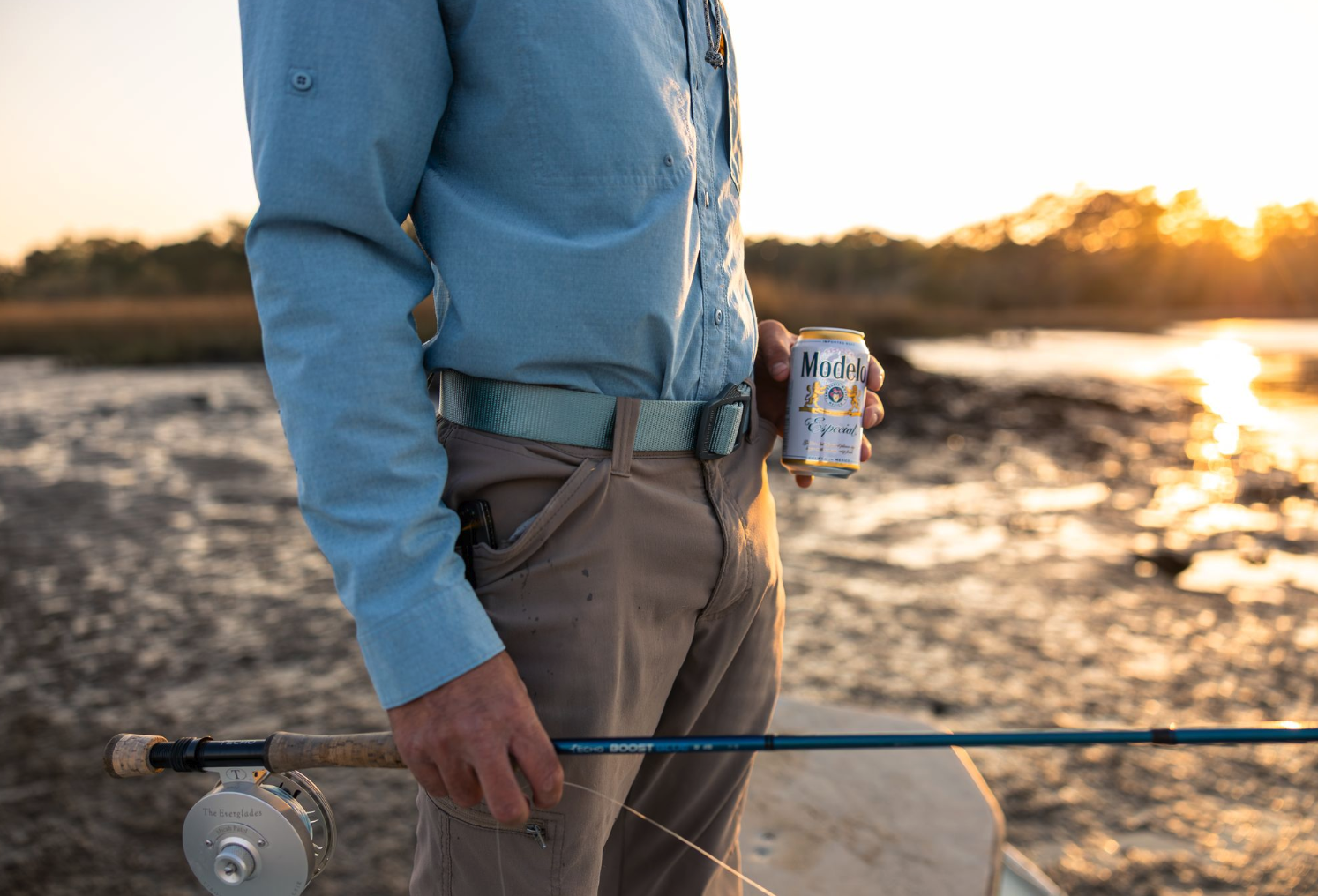 Man holding fly rod and beer wearing Fishpond Dorsal Fin Webbing Belt