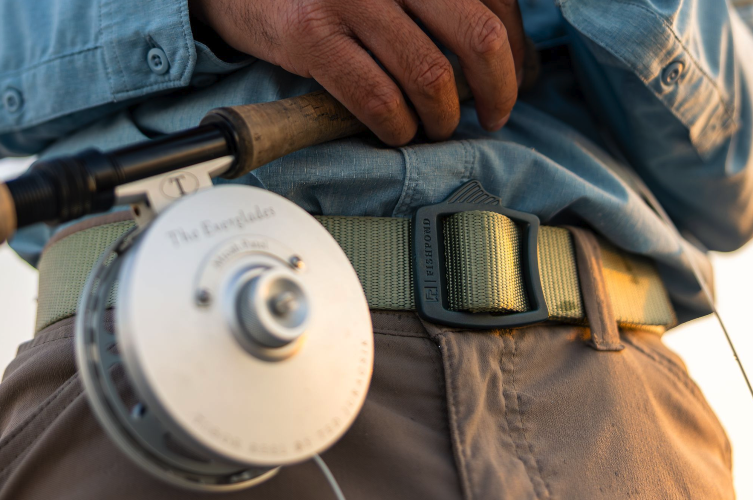 Close up of green Fishpond Dorsal Fin Webbing Belt on man holding fly rod and reel