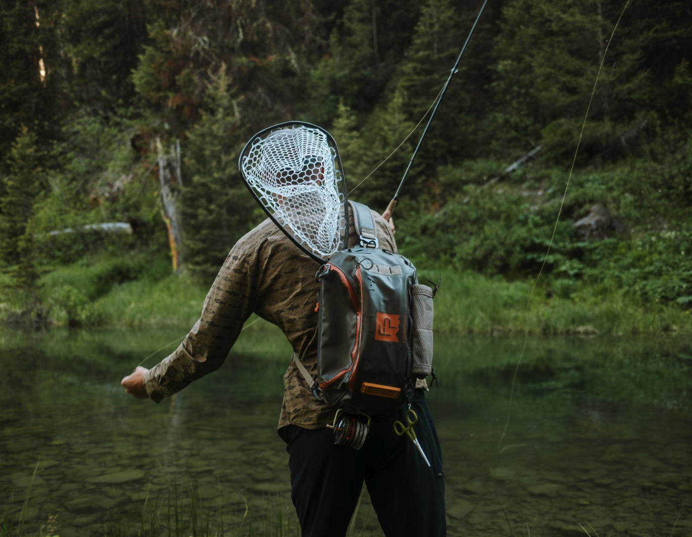 Angler fishing with Fishpond Nomad Canyon Net Colorado Cutty in sling pack