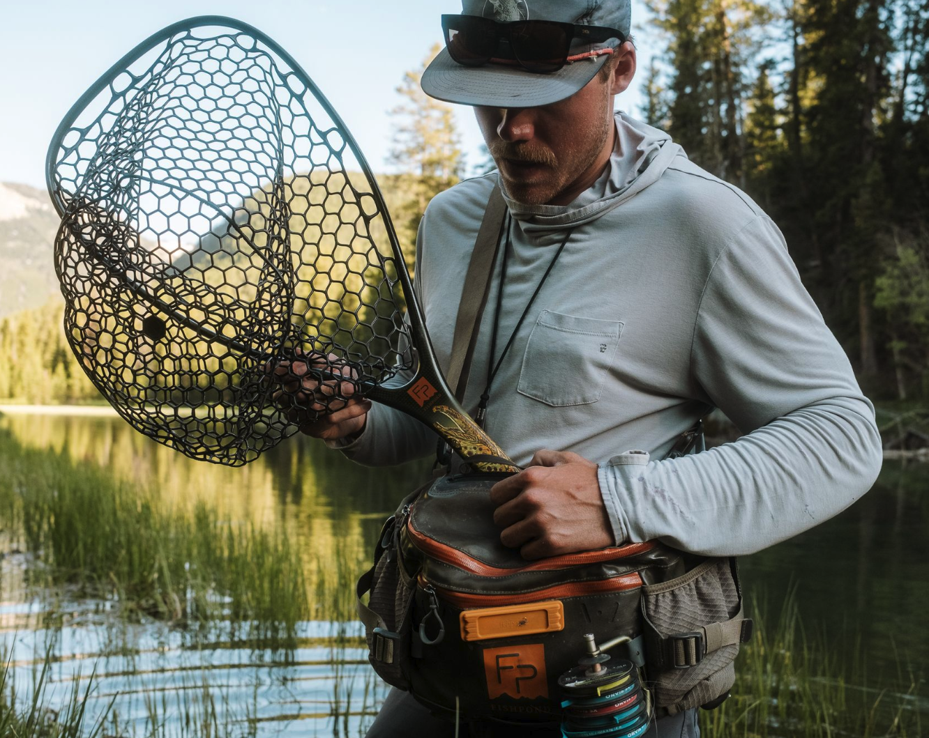 Angler holding Fishpond Nomad Middle Fork Net Hook Jaw Limited Edition by hip pack