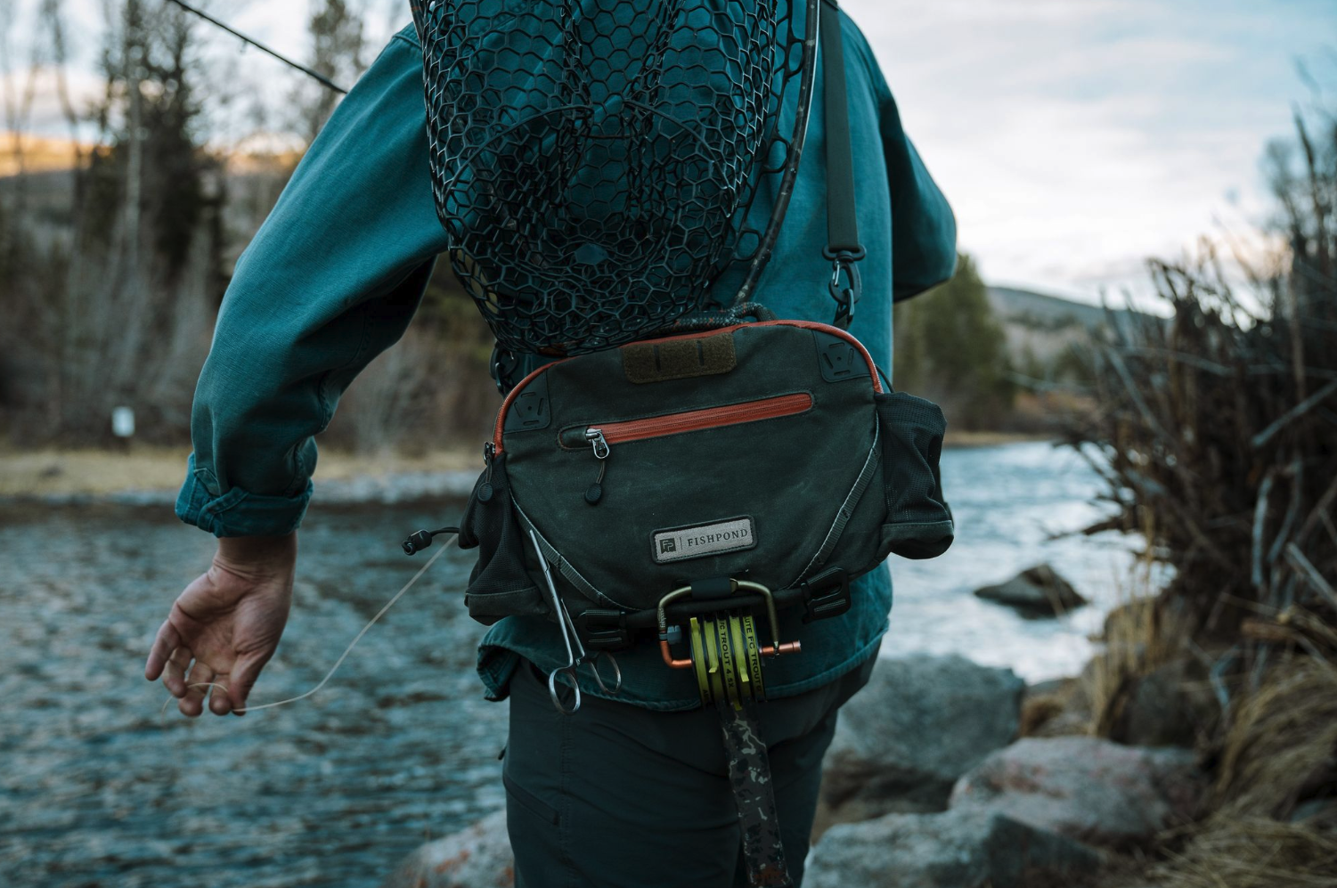 Man fishing with net in holster of Fishpond Elkhorn Lumbar Pack Duskwood Waxed Cotton