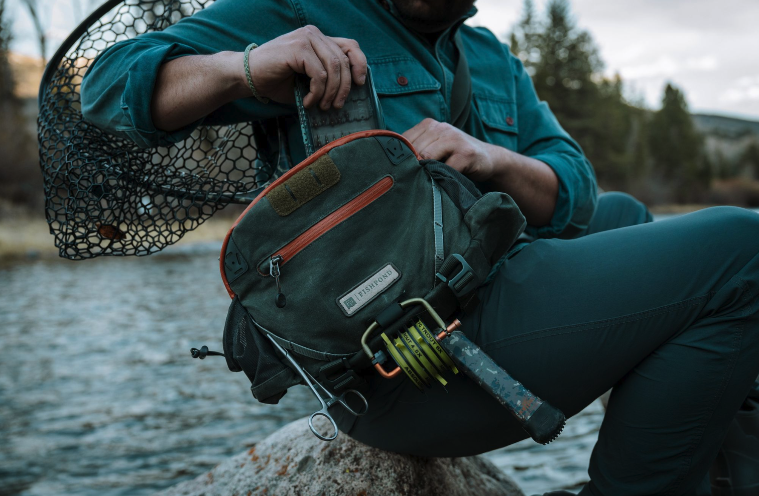 Angler wearing Fishpond Elkhorn Lumbar Pack Duskwood Waxed Cotton zipping it open