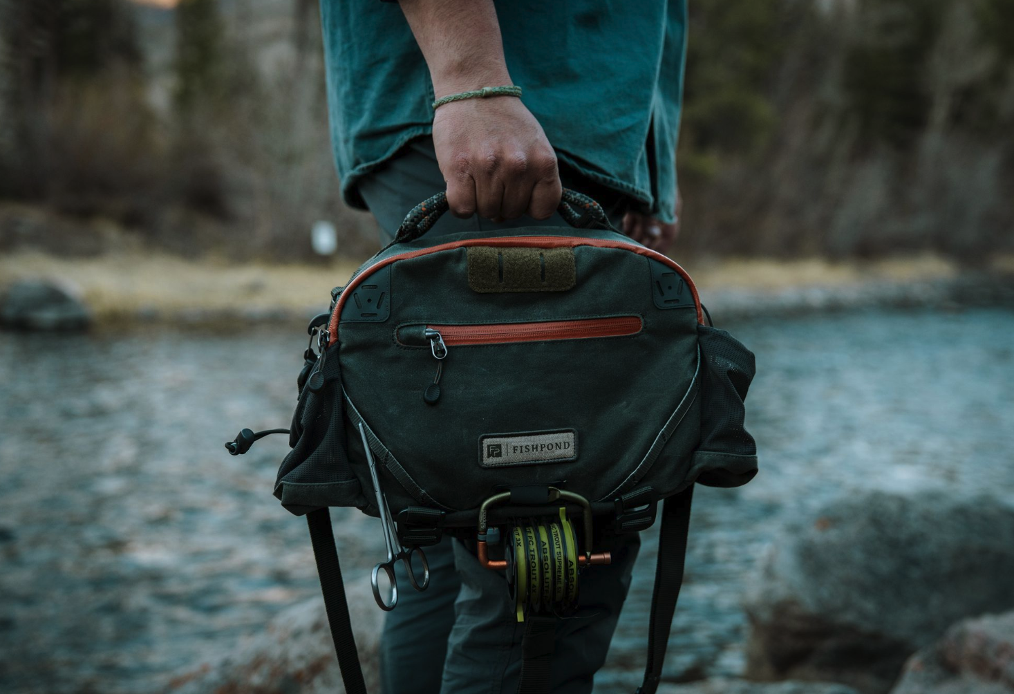 Man holding top strap of Fishpond Elkhorn Lumbar Pack Duskwood Waxed Cotton