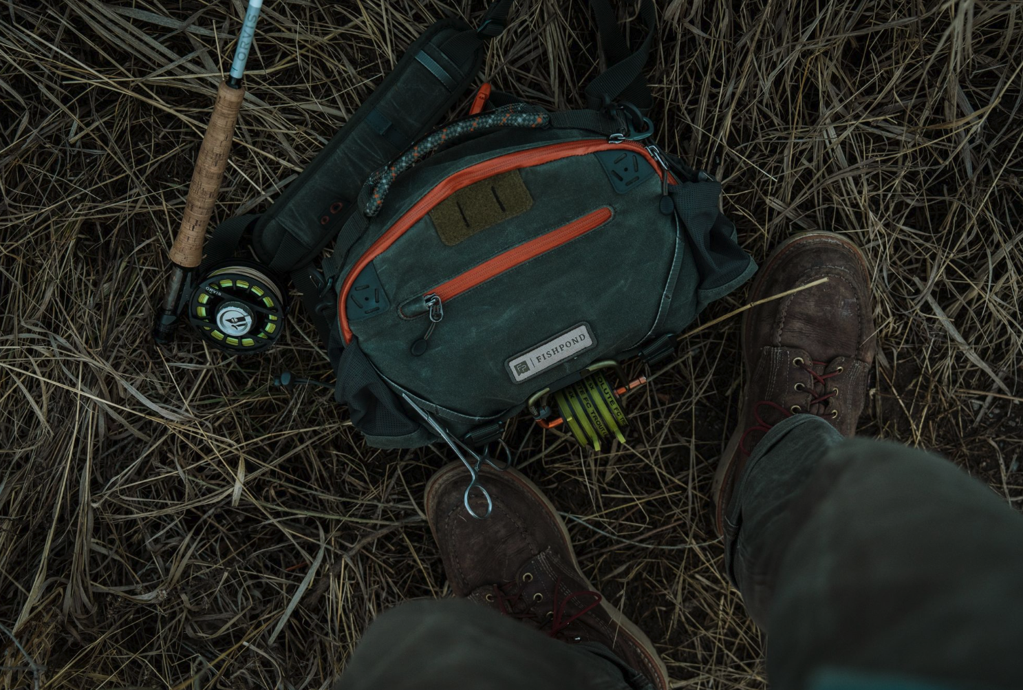 Fishpond Elkhorn Lumbar Pack Duskwood Waxed Cotton on ground with fly rod and reel