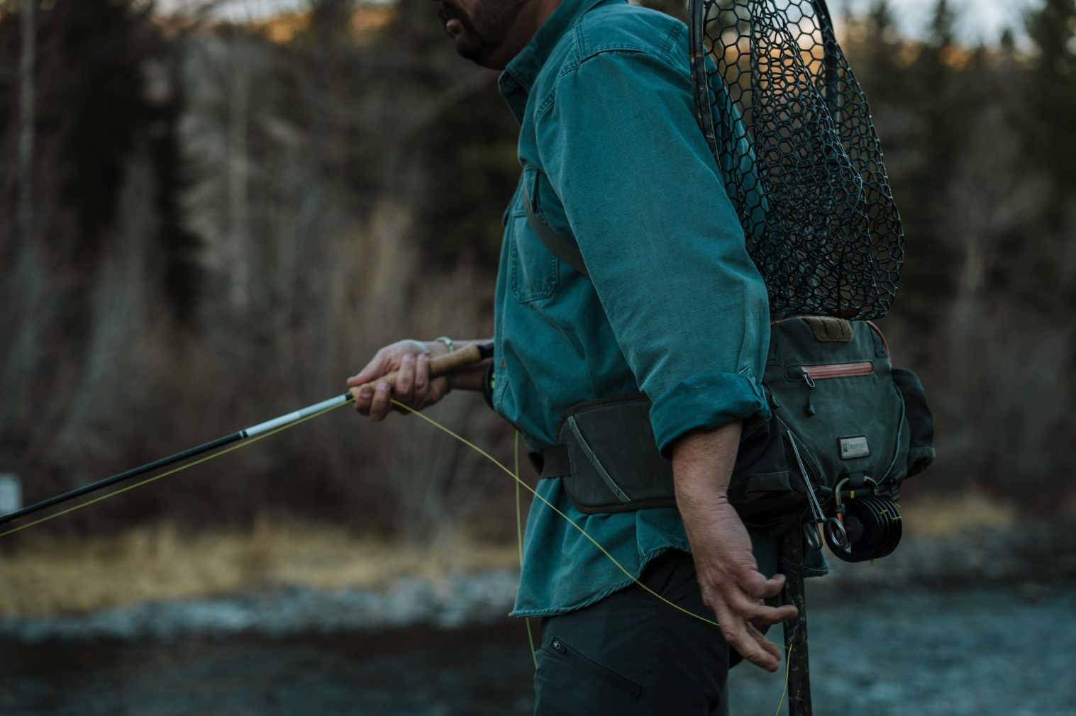 Angler fly fishing while wearing Fishpond Elkhorn Lumbar Pack Duskwood Waxed Cotton