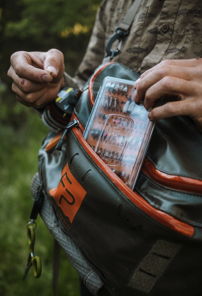 Angler putting  Tacky Original Fly Box Burnt Orange into hip pack
