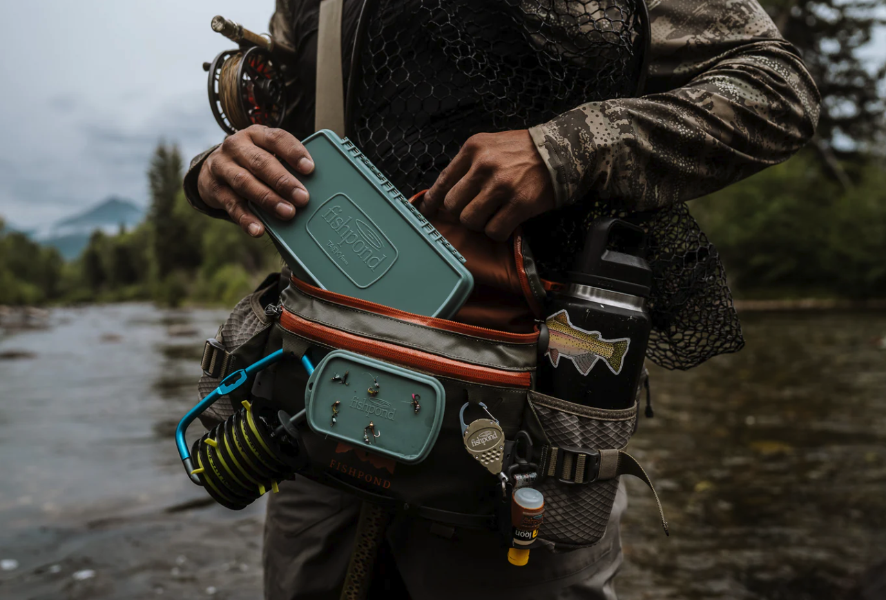Angler putting Fishpond Tacky Pescador Dynamic Foam Fly Box Large into hip pack on river