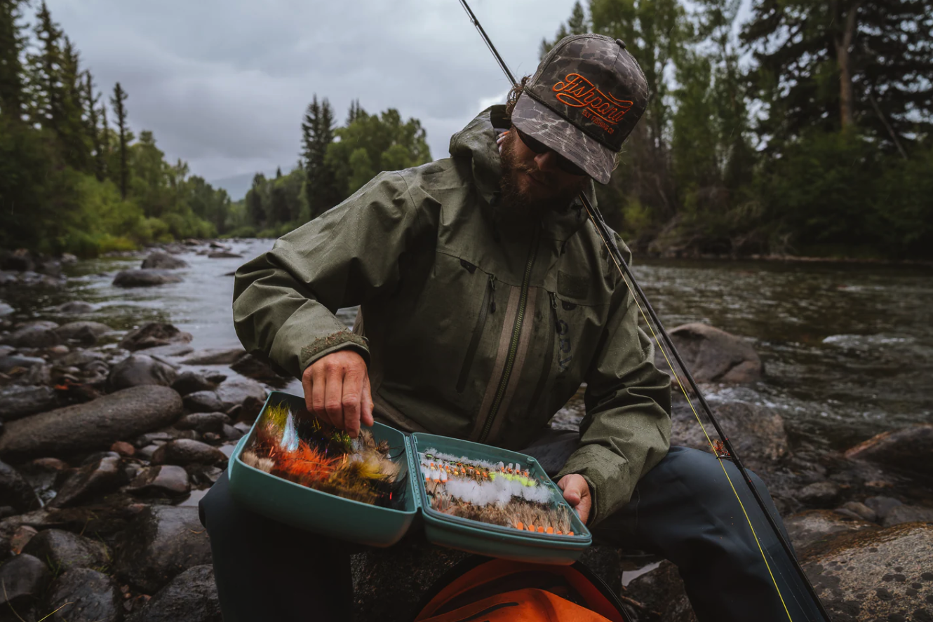 Angler sitting in river selecting a fly from Fishpond Tacky Pescador Dynamic Foam Fly Box XL