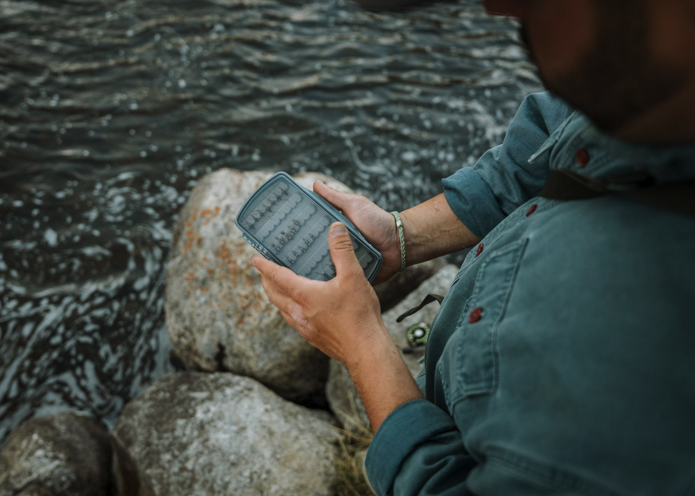 Angler holding Fishpond Tacky Pescador LowPro Clear Medium Fly Box near river