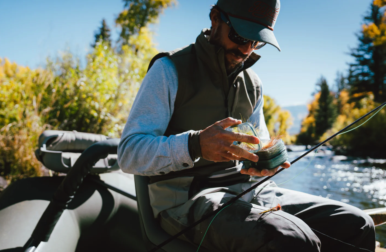 Angler in drift boat selecting flies from Fishpond Tacky Predator Fly Puck