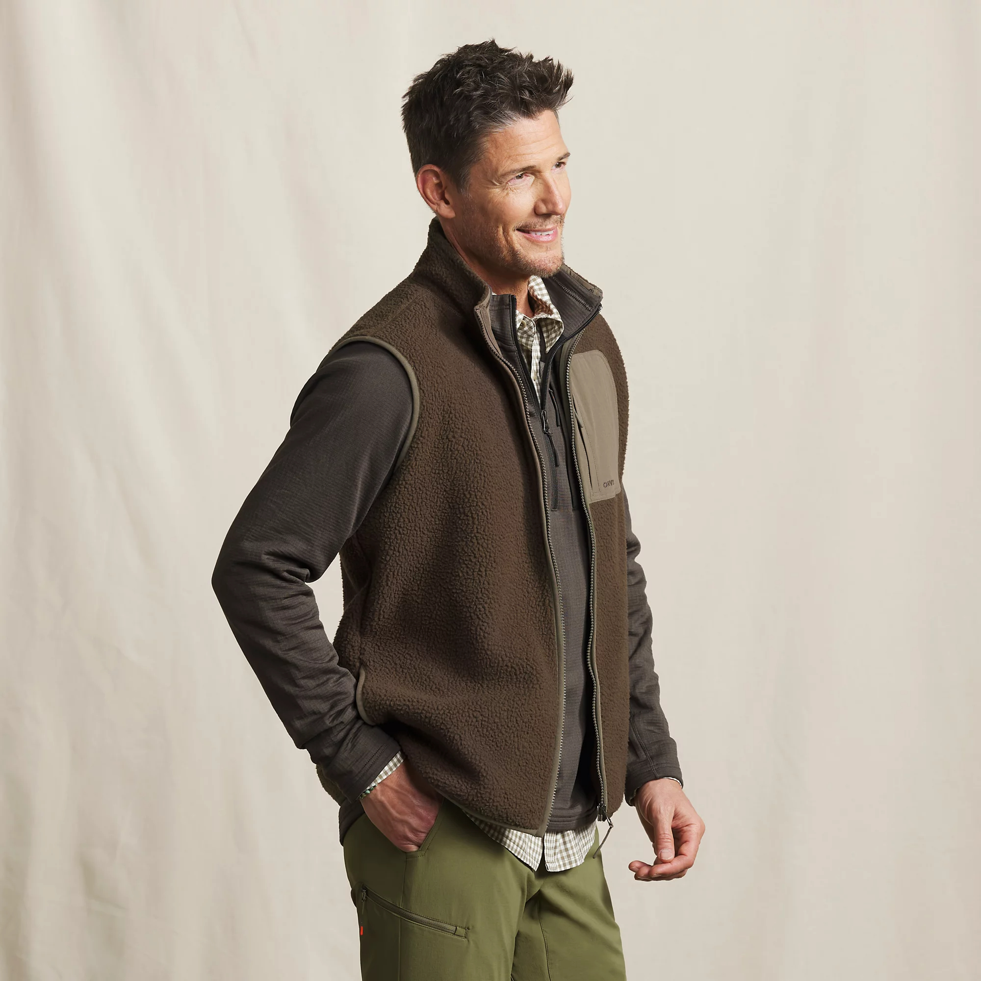 Man wearing brown Orvis Mad River sherpa fleece vest over a long-sleeve shirt for fishing, camping, and outdoor layering.