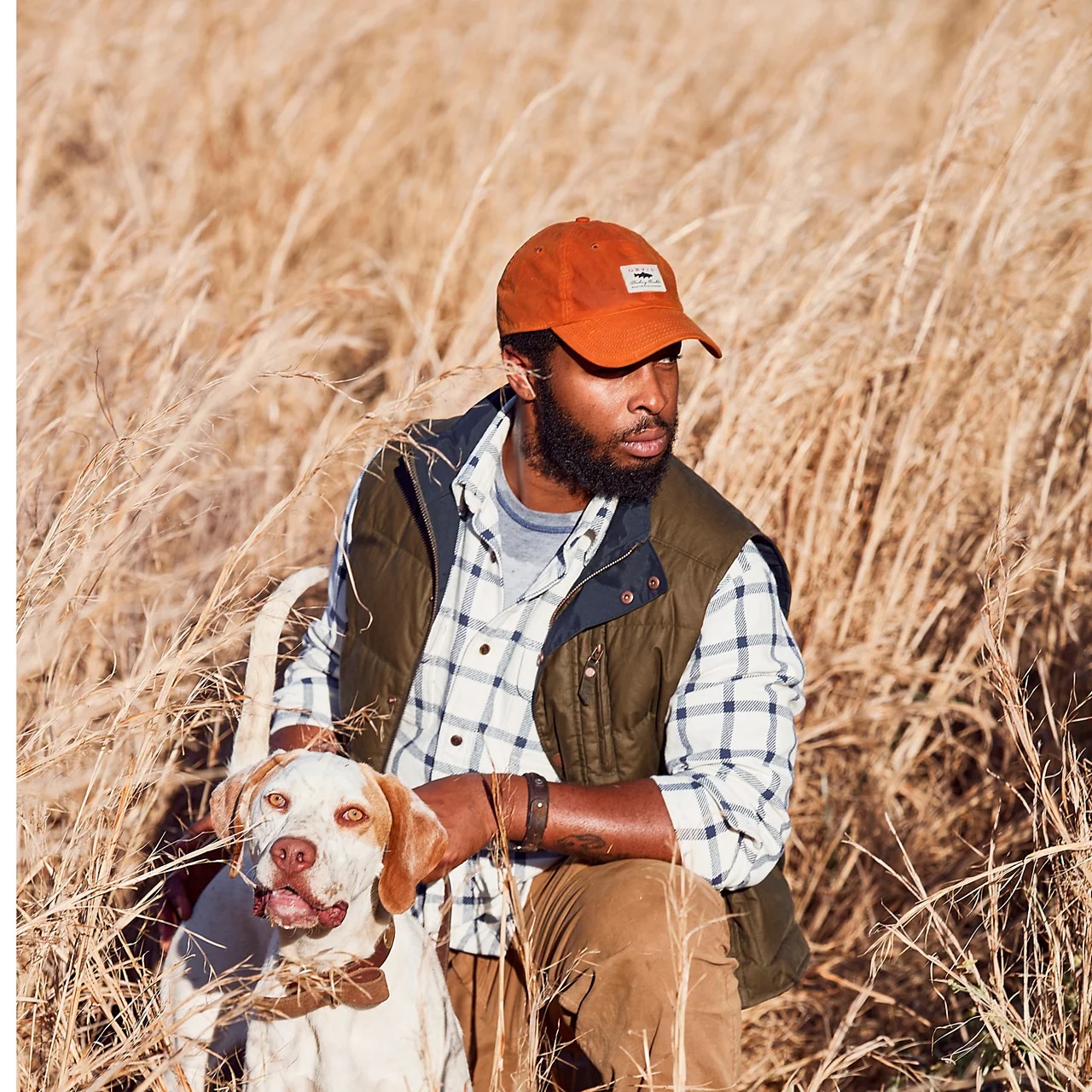 Orvis Vintage Waxed Cotton Ball Cap Burnt Orange outdoor fishing cap worn by man with dog in tall grass