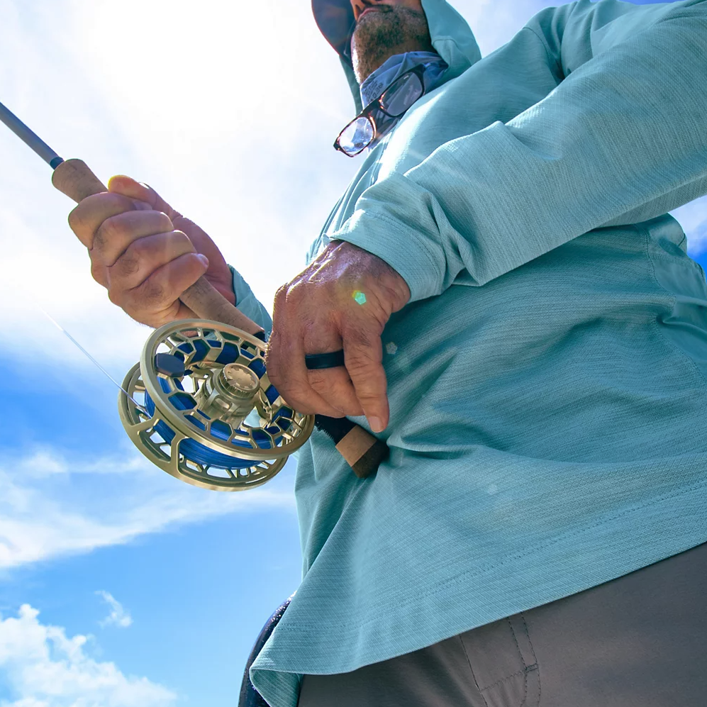 Angler reeling in line with Orvis Ratio Fly Reel Gold color