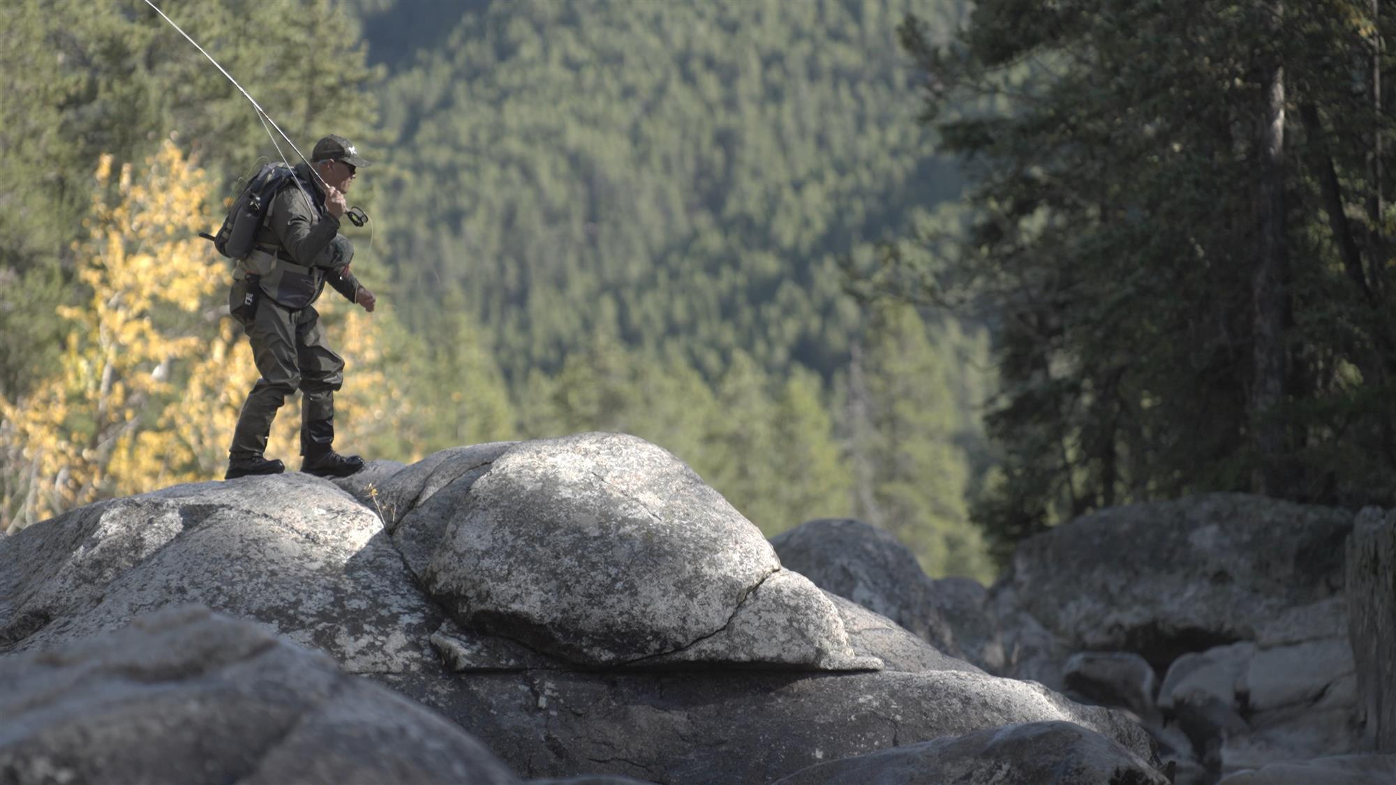 A fly fisherman walking across rocks on a river