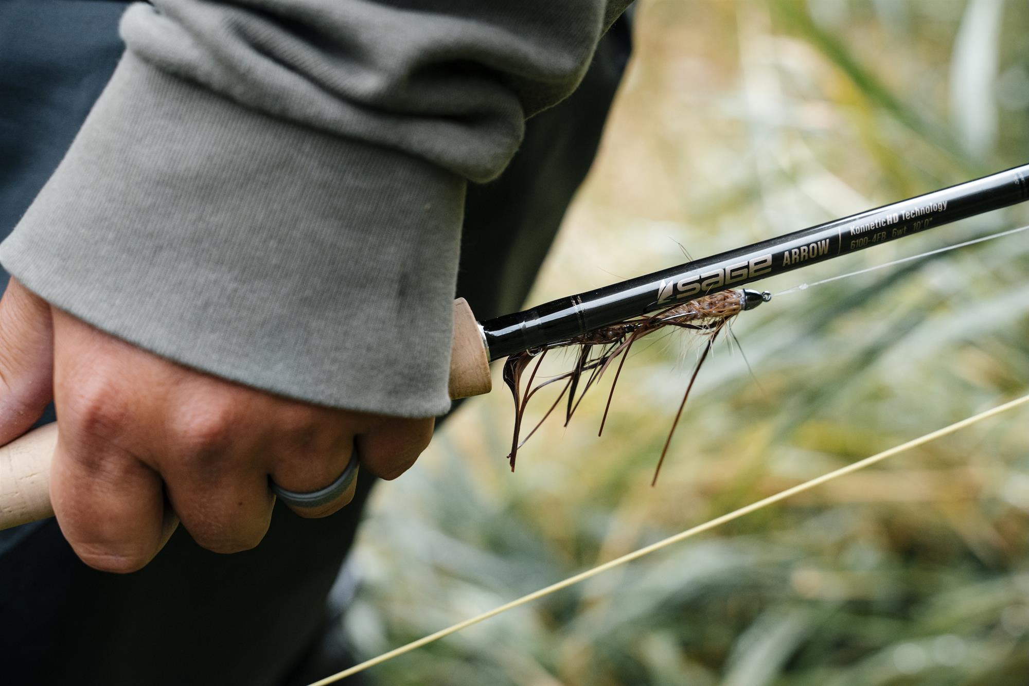 Close up of hand carrying Sage ARROW Fly Rod with fly