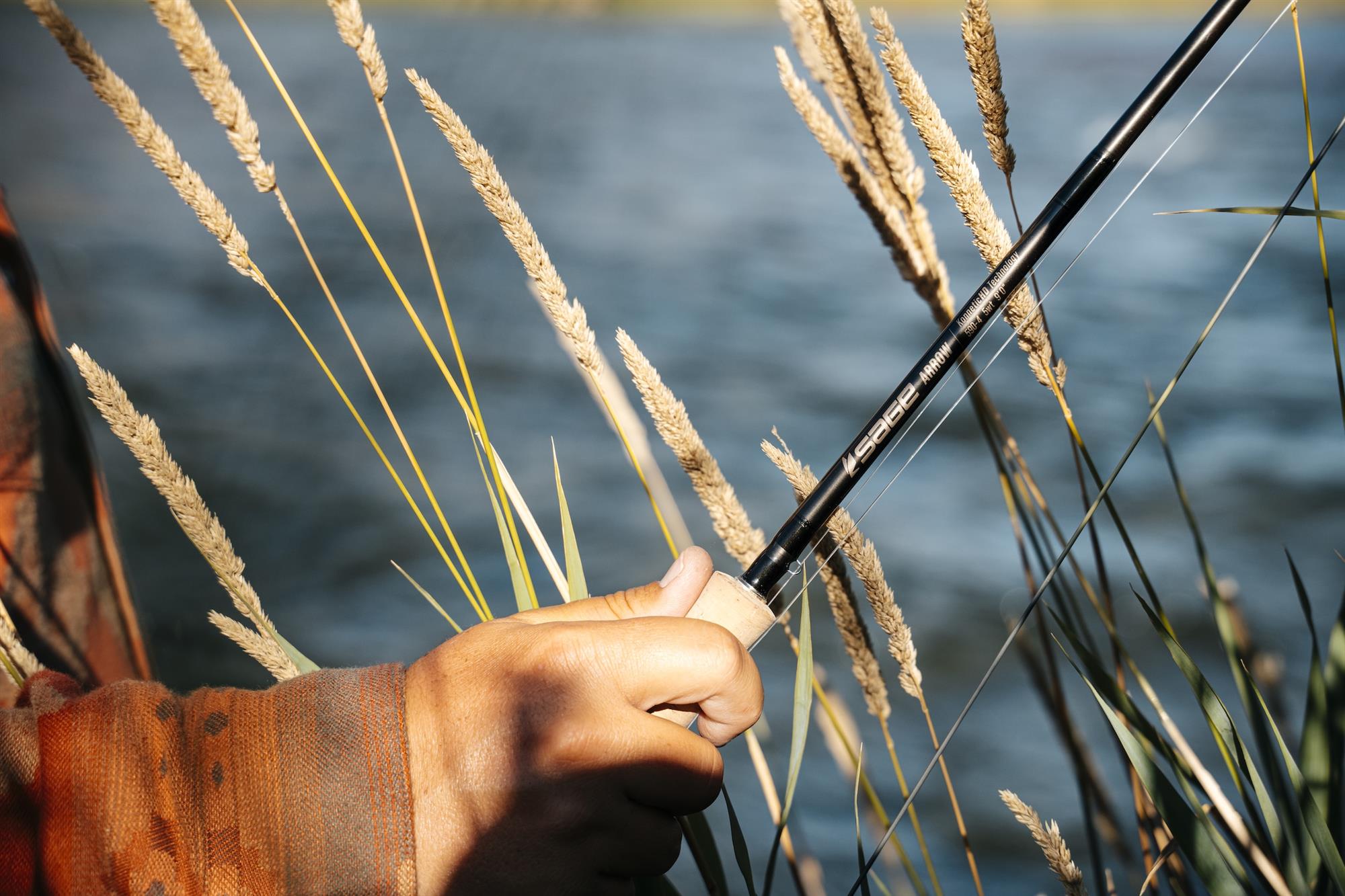 Angler holding up Sage ARROW Fly Rod in grass