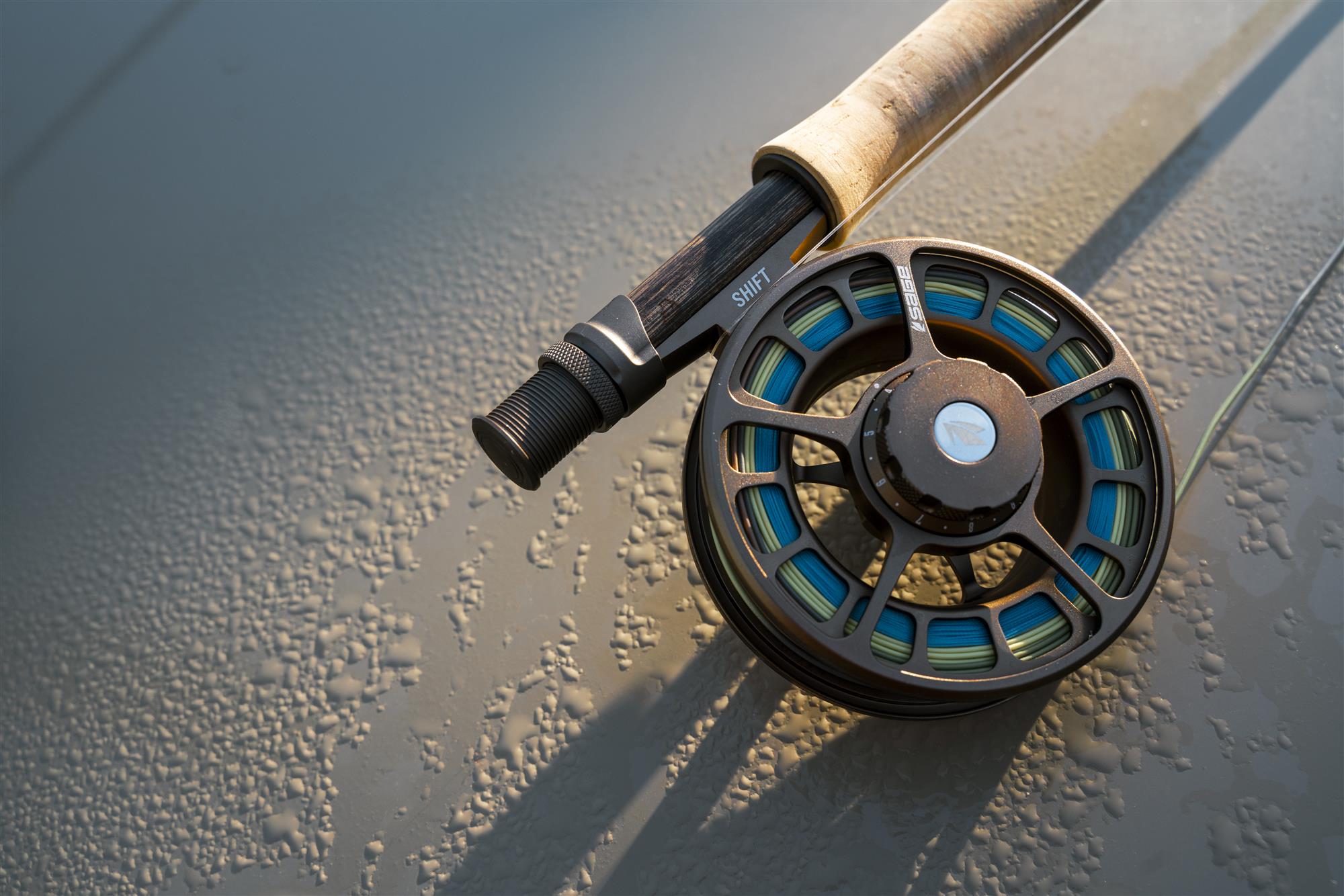 Sage SHIFT fly fishing reel mounted on a fly rod lying on a wet drift-boat deck with water droplets in warm evening light