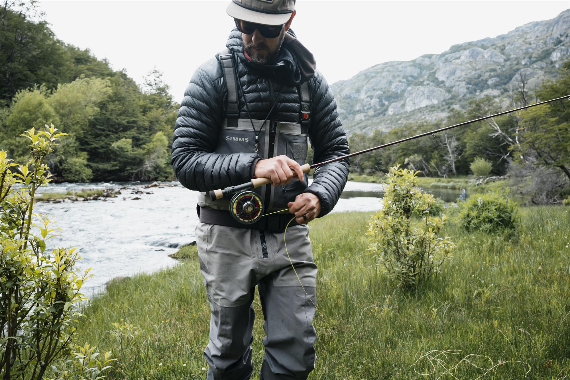 Angler rigging a fly rod riverside with Sage SHIFT LT fly fishing reel—lightweight sealed-drag reel for trout fishing