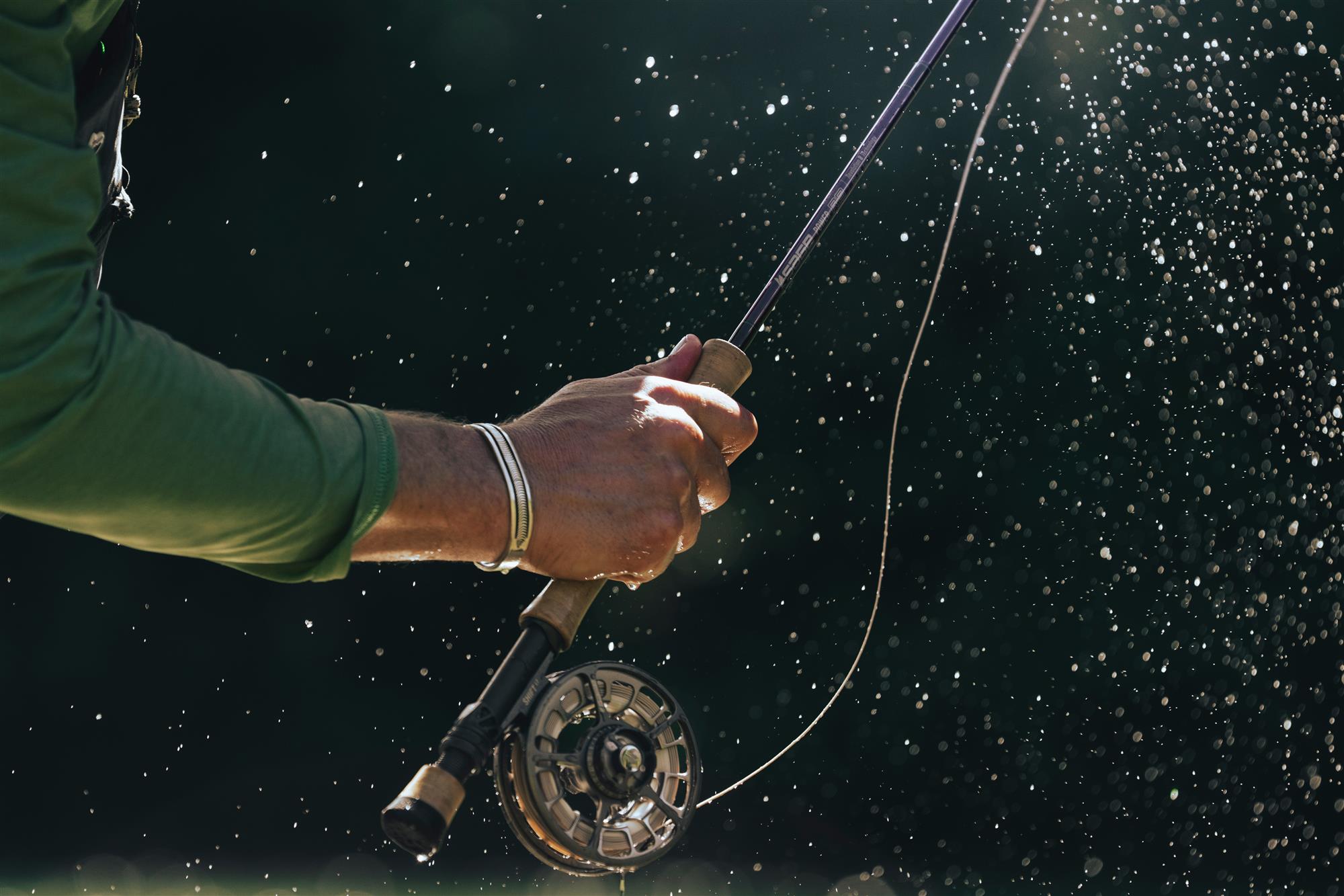 Close-up of fly rod grip and Sage SHIFT LT fly fishing reel during casting with water spray—performance fly reel action shot
