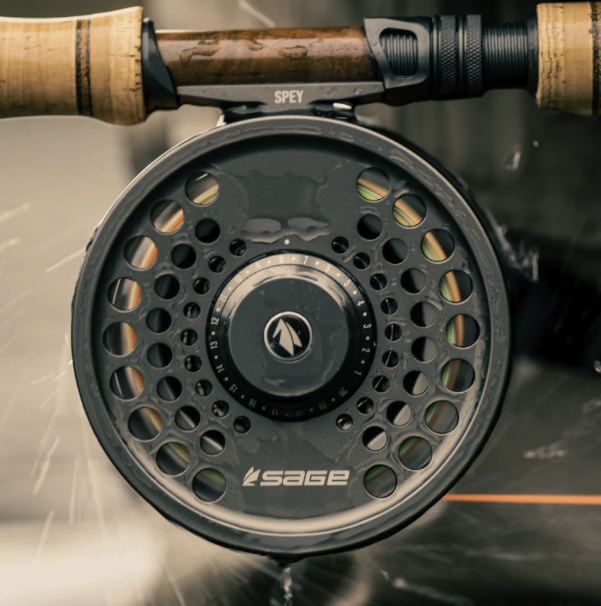 Sage SPEY 2 Reel mounted on a spey rod, set against a backdrop of lush greenery, ideal for salmon and steelhead fishing.