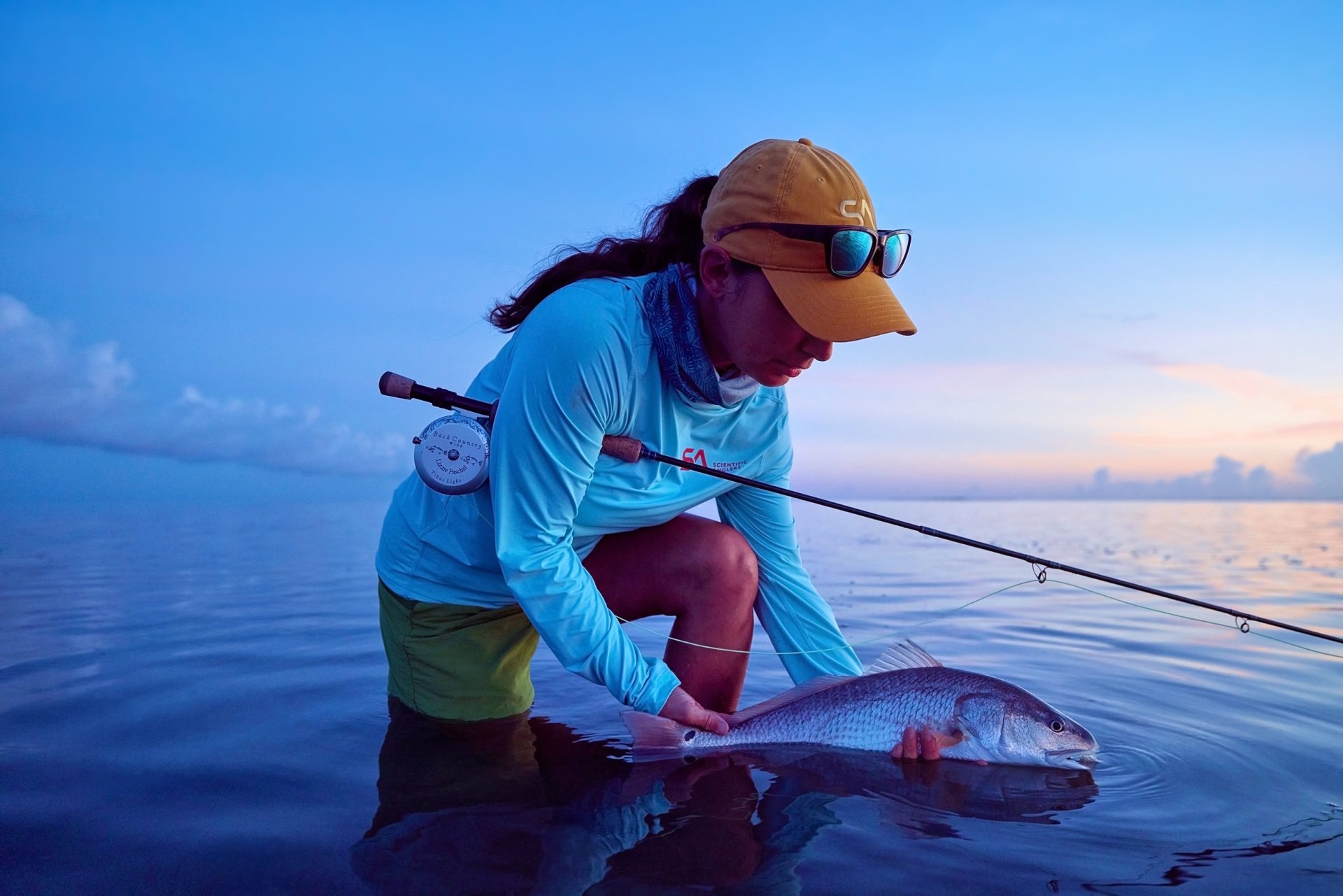 Scientific Anglers Low Profile Hat Yellow fly fishing cap worn by angler while releasing a redfish