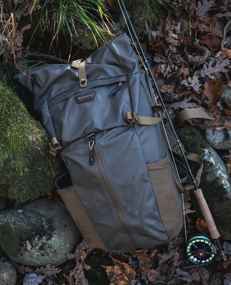 Simms Headwaters Backpack next to fly fishing rod on rocks.