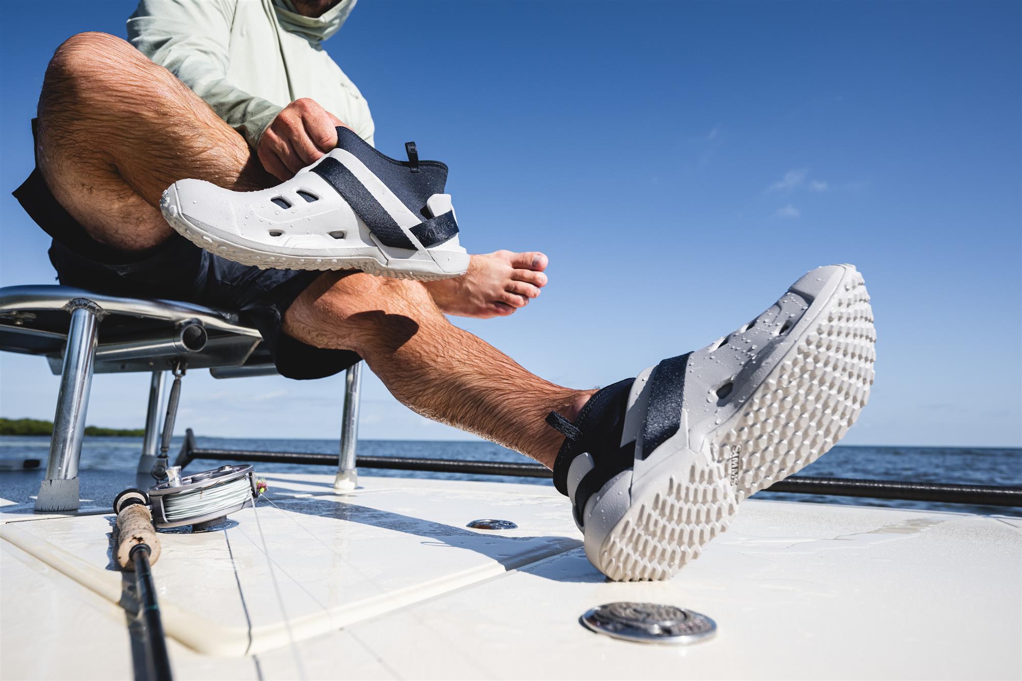 Angler putting on Simms Drifter AT wet wading shoes on boat deck showing adjustable strap and traction outsole