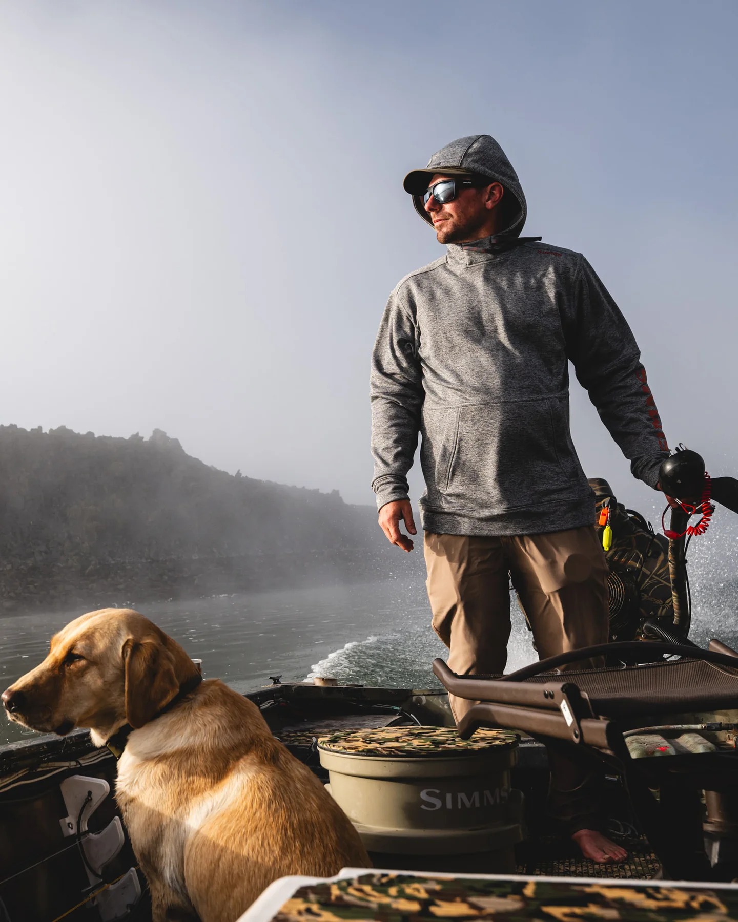 Angler Driving A Boat Wearing A Simms Challenger Hoody