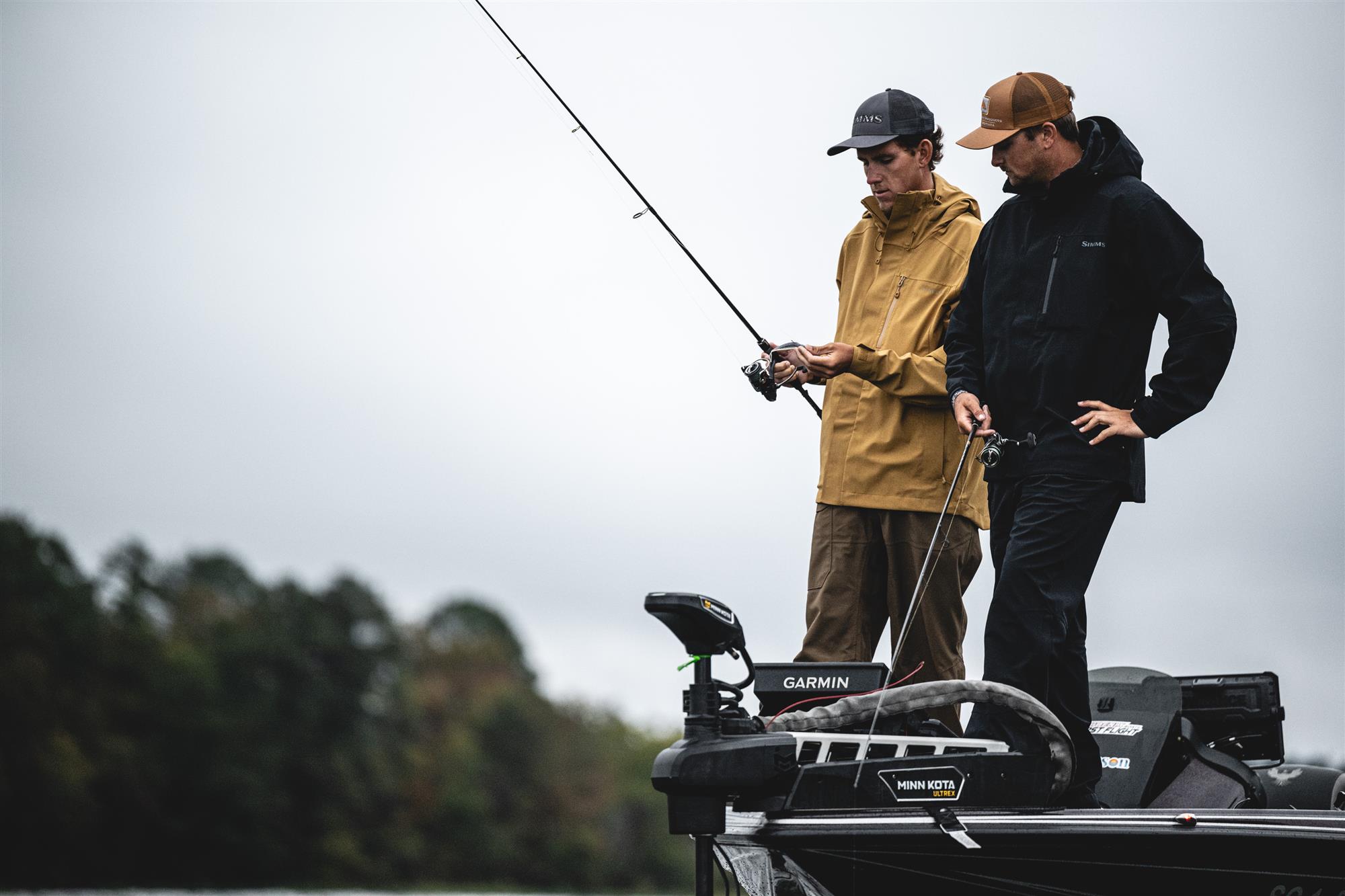 Simms Challenger waterproof fishing rain jacket worn by anglers on bass boat in rainy weather