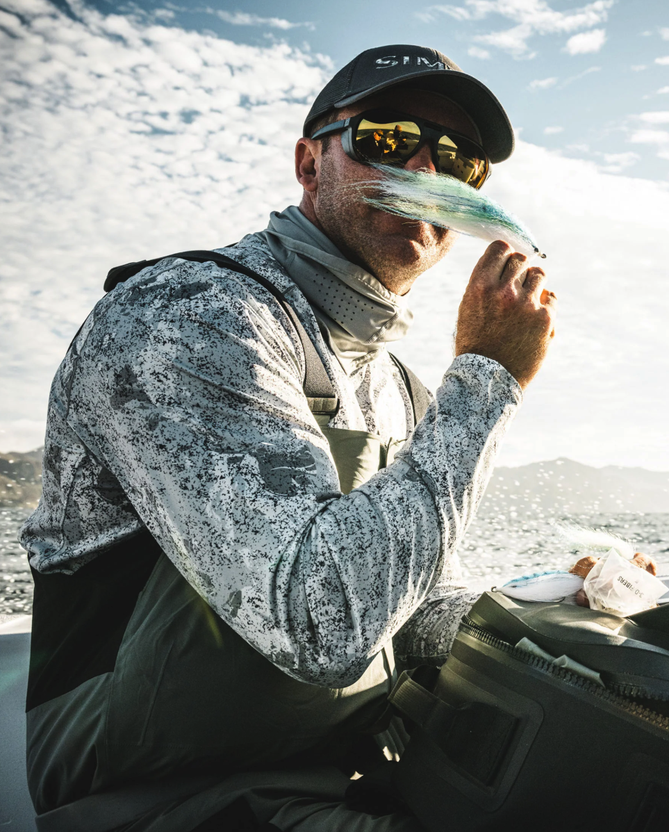 Angler wearing Simms BugStopper SolarFlex Hoody holding up a fly.