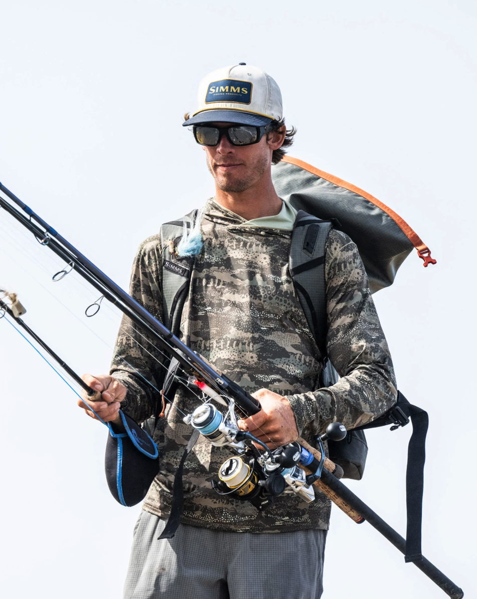 Angler wearing Simms BugStopper SolarFlex Hoody and carrying fishing rods.