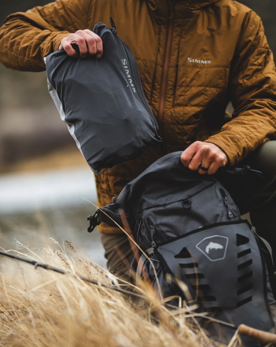 Man putting Simms Flyweight Packable Waders in backpack