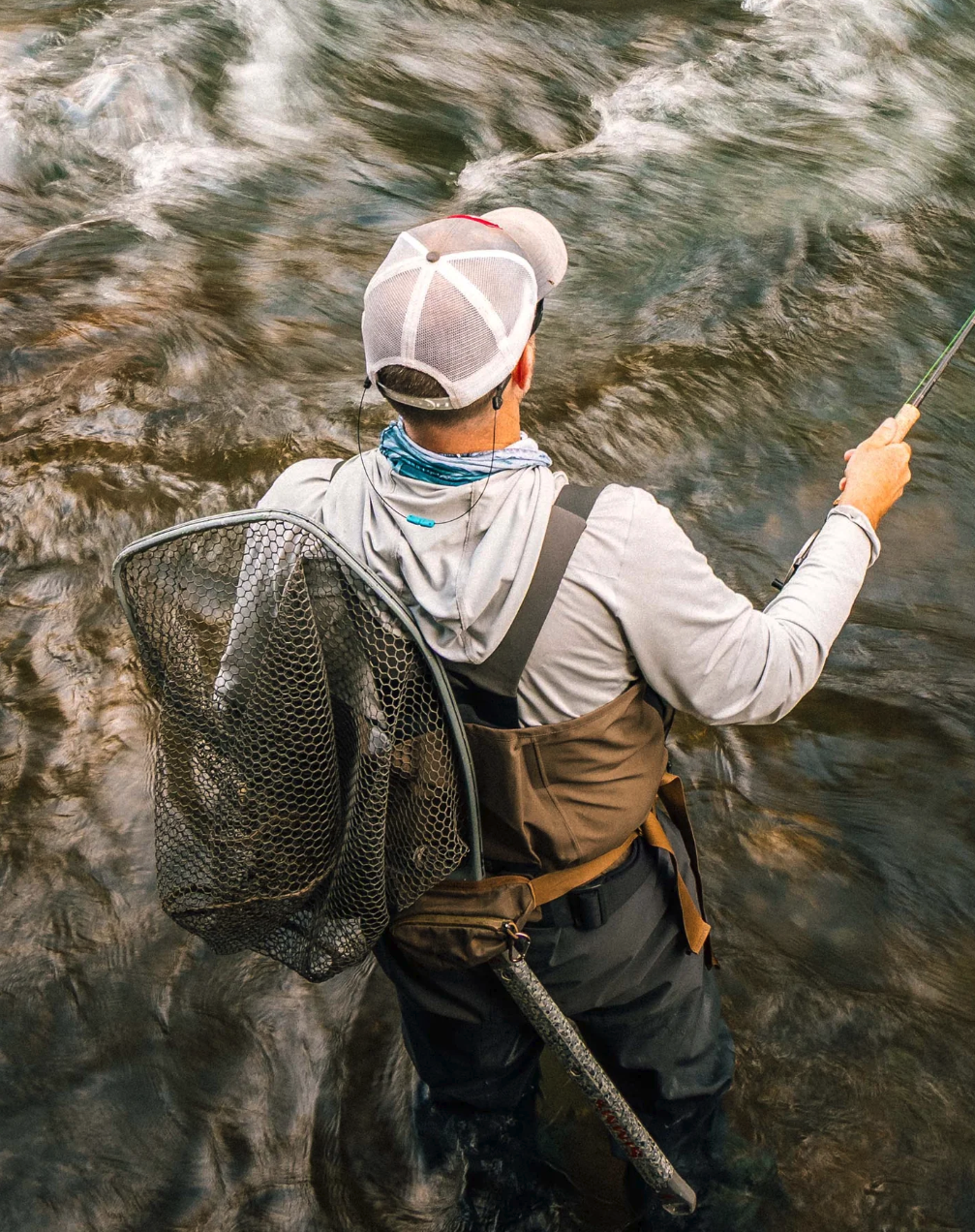 Fly angler wearing Simms G3 Pro Guide chest waders while casting in a flowing river with a landing net