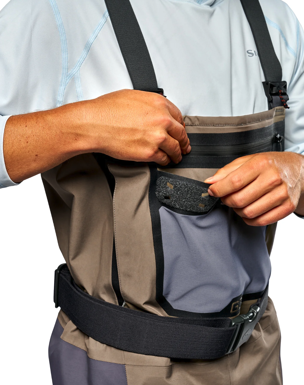 Angler demonstrating the front chest pocket and accessory docking patch on Simms G3 Pro Guide fishing waders