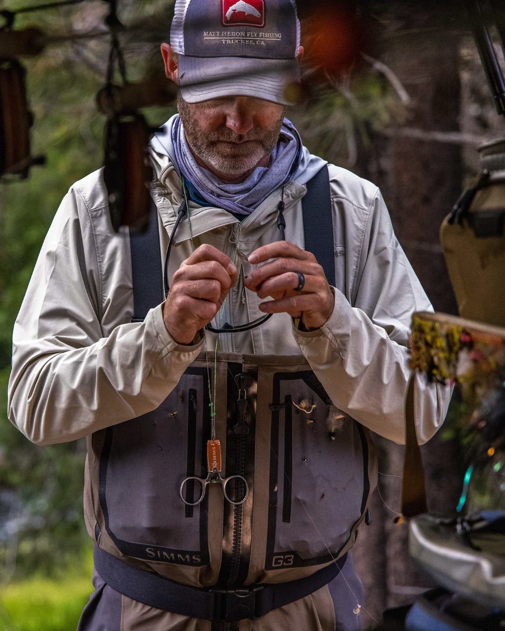 Fly angler wearing Simms G3Z Pro Guide zippered waders while preparing fishing tackle beside a river