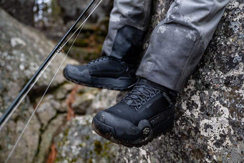 Angler wearing Skwala RS wading boots while sitting on rocky river bank during fly fishing trip