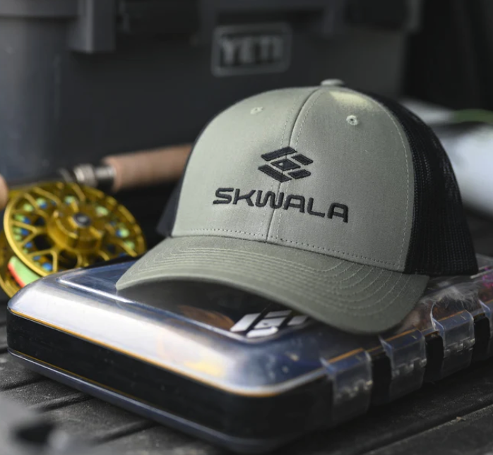 Skwala Icon Mid Trucker Hat on fly box next to fly rod and reel