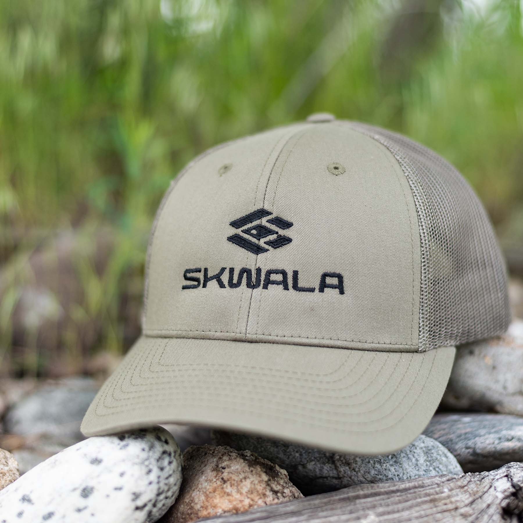 Skwala Icon Mid Trucker Hat Set On Rocks Of A River Bank