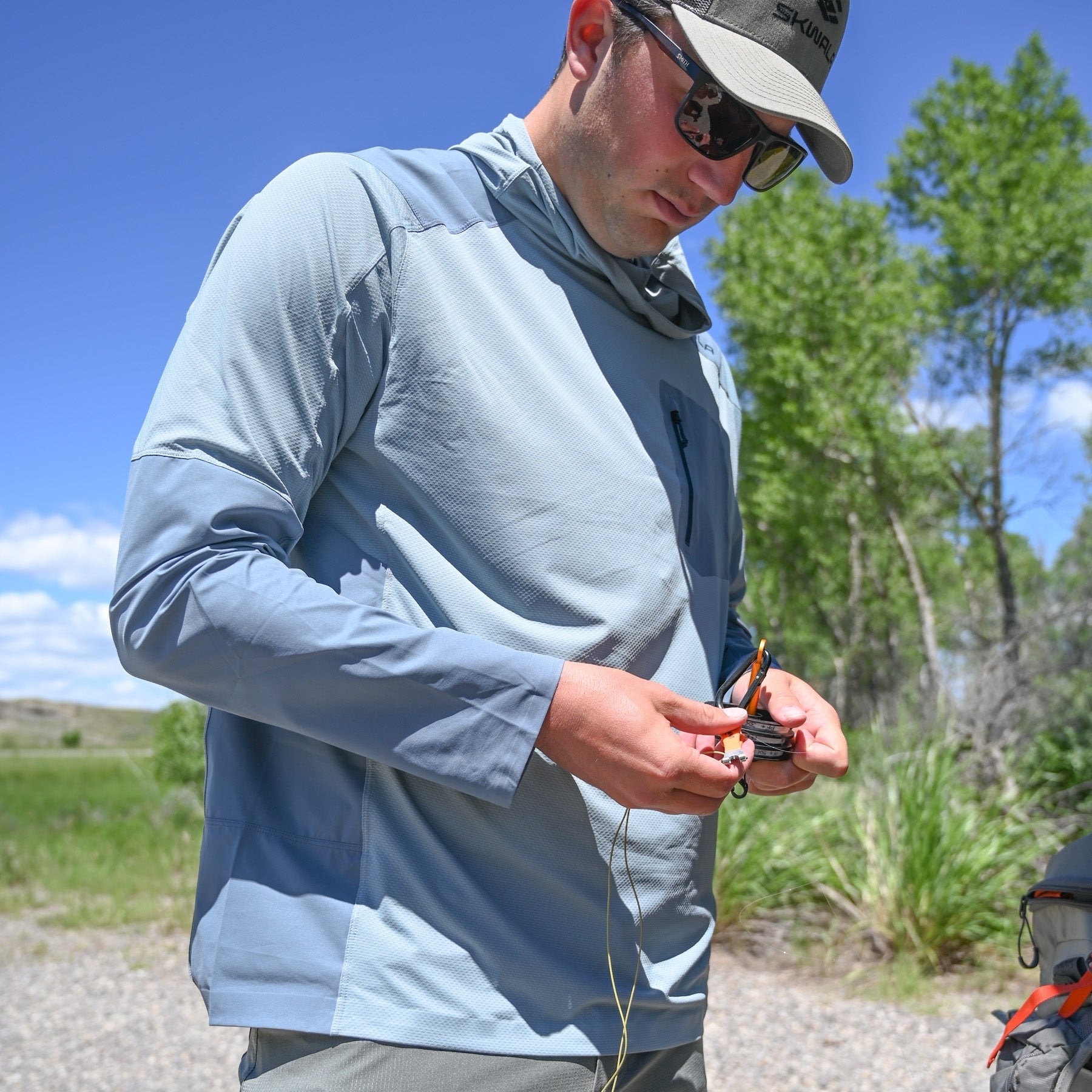 Angler wearing Skwala Sol Tactical Hoody lightweight UPF fly fishing sun shirt while rigging tackle on riverbank