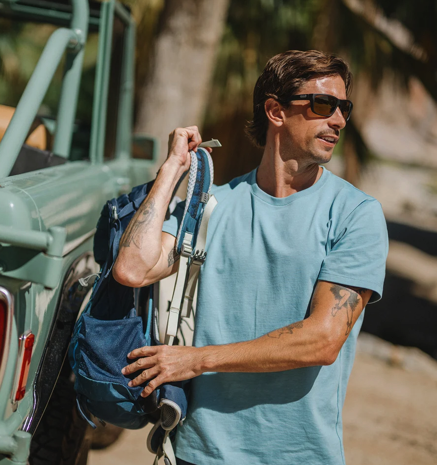 Man wearing Suncloud Mayor Polarized Sunglasses Matte Black Sienna Mirror putting on backpack