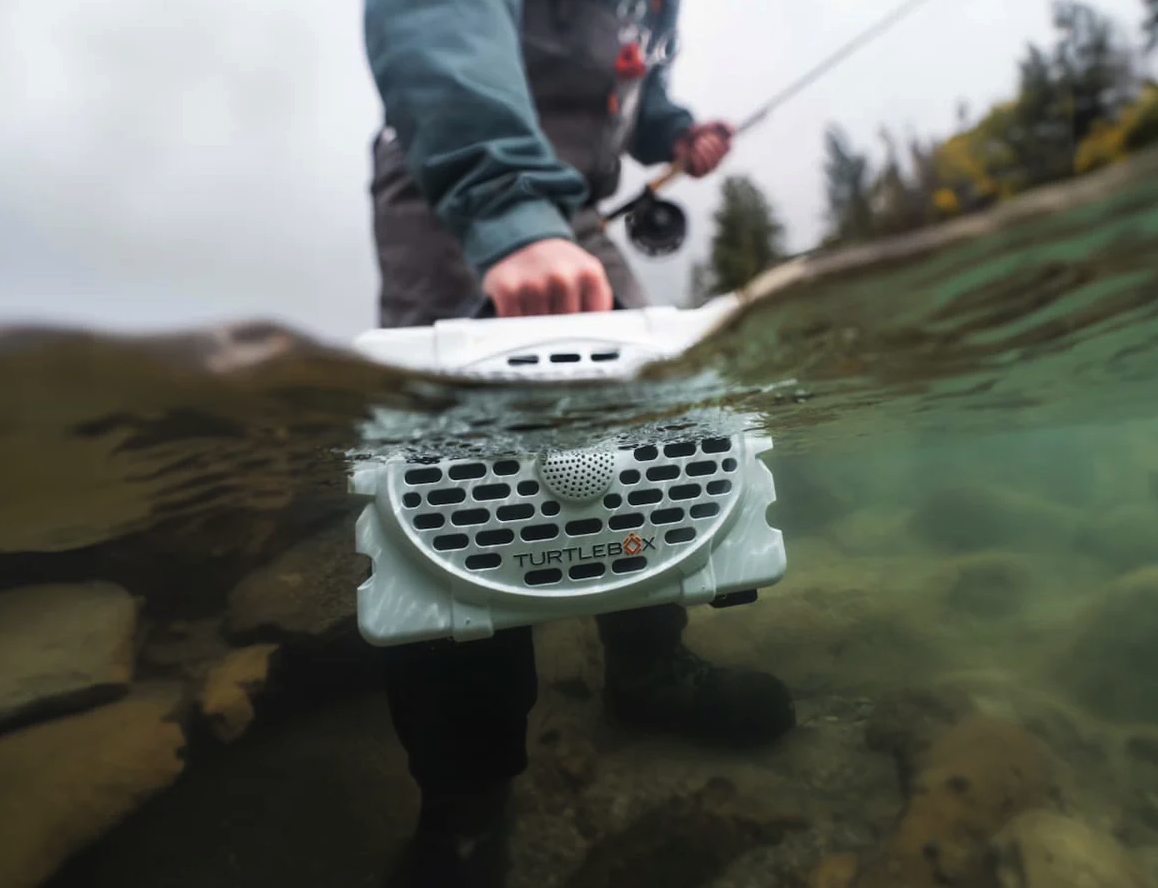 Fly fisherman holding Turtlebox Original Speaker in water.