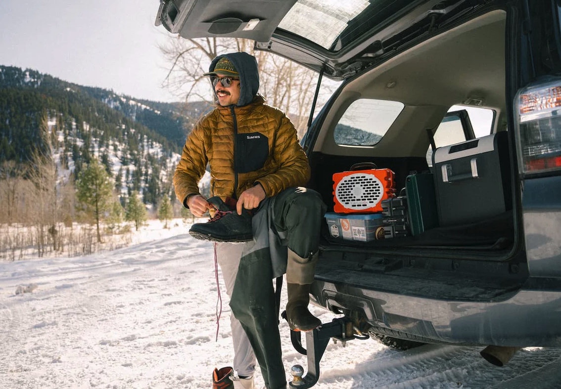 Fly fisherman putting wading boots on with Turtlebox Original Speaker in back of truck