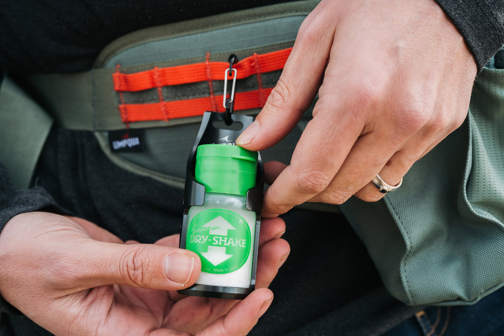 Angler using an Umpqua RiverRun Shake Floatant Holder attached to a fly fishing pack for quick dry fly powder access