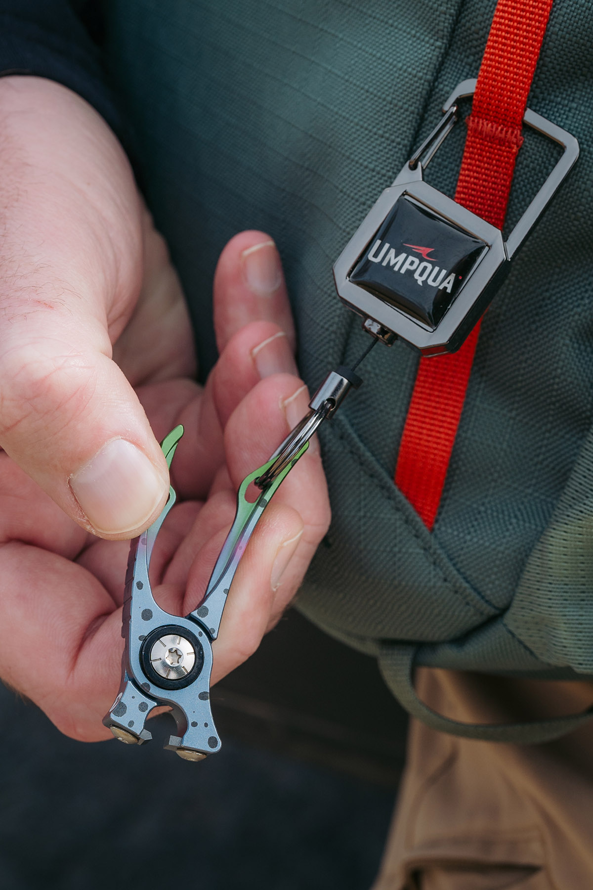 Angler using the Umpqua RiverRun Small Retractor with fly fishing nippers attached to a pack strap