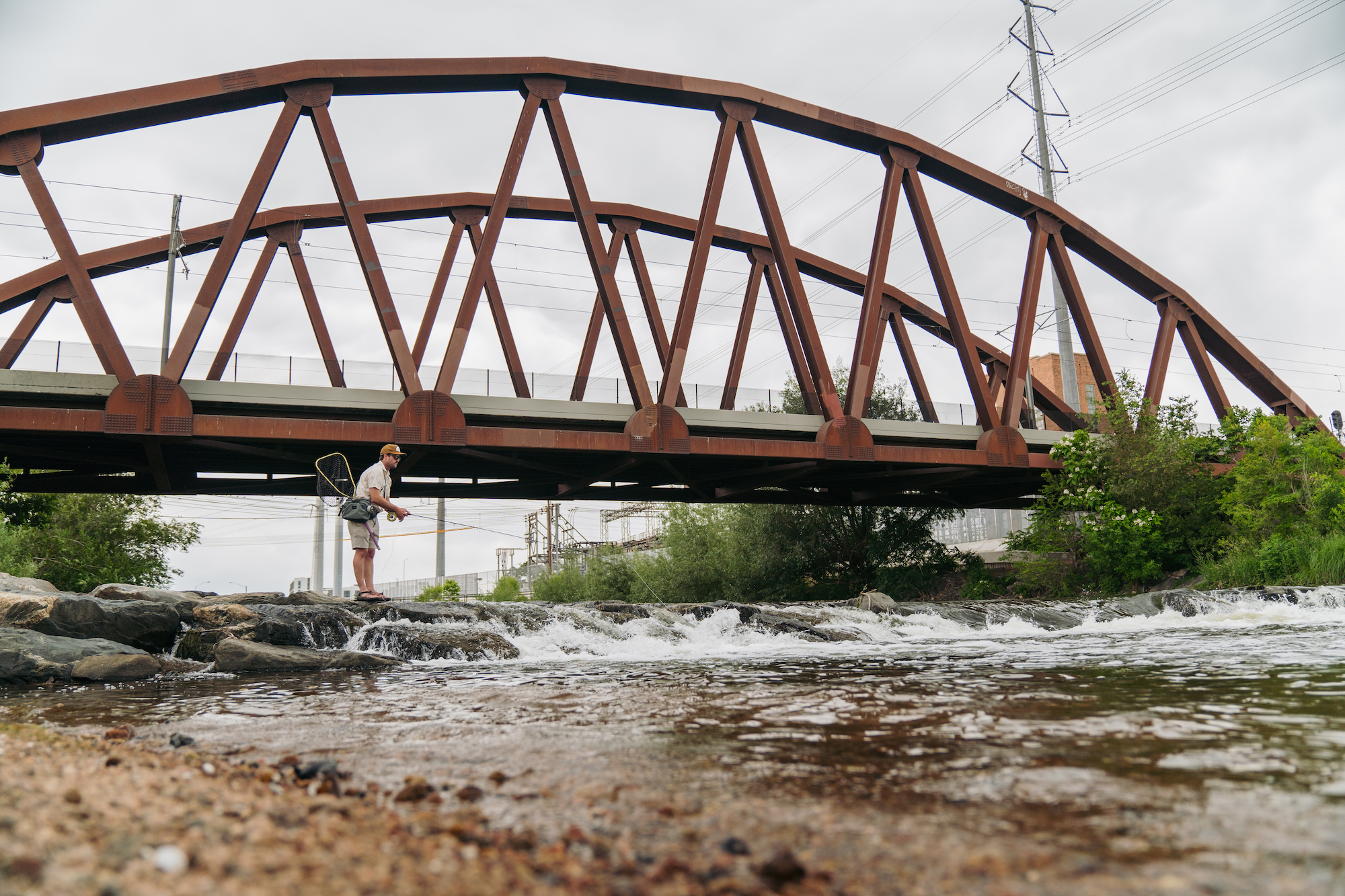 Umpqua SWIFTLINK Ledges waist pack fly fishing angler standing on river rocks under steel bridge casting fly rod