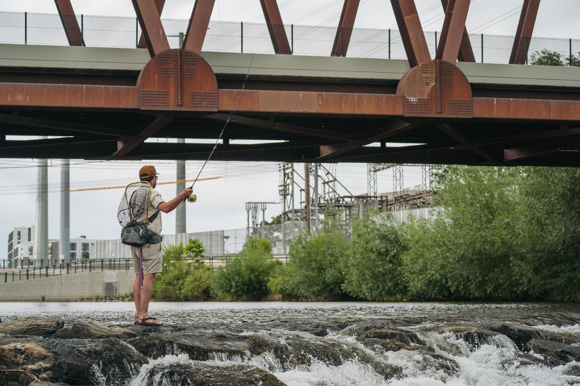 Angler fly fishing in river wearing Umpqua SWIFTLINK waist pack casting under bridge high capacity fishing waist pack