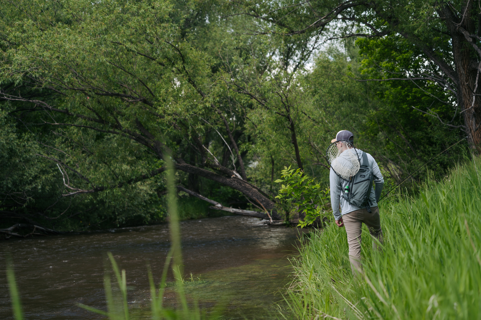 Fly angler hiking along river wearing Umpqua Steamboat sling pack with net attached high capacity fly fishing gear pack
