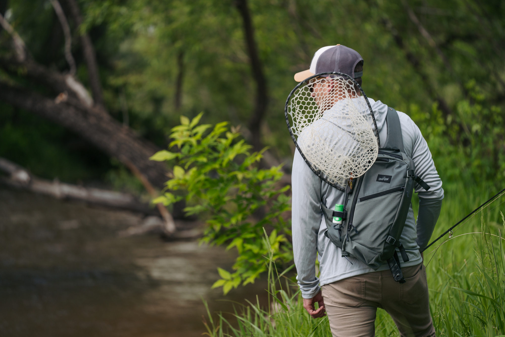 Rear view angler wearing Umpqua SWIFTLINK Steamboat sling pack with landing net streamside trout fishing setup