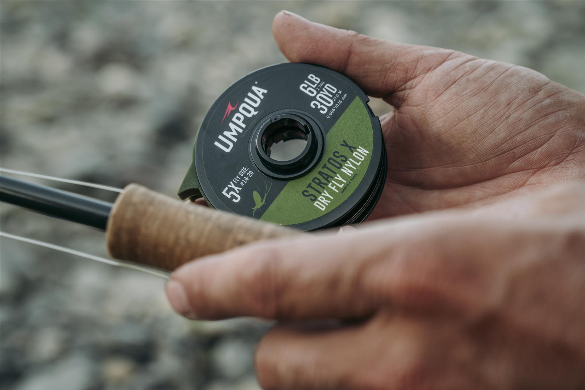 An angler holding a spool of Umpqua Stratos X Dry Fly Tippet next to his fly rod